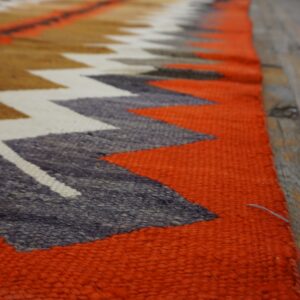 Coarse textured rug with bright orange and multi-colored chevron patterns rests on wood flooring.