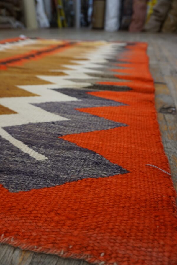 Coarse textured rug with bright orange and multi-colored chevron patterns rests on wood flooring.