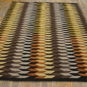 Geometric flatweave rug in brown, yellow, black, and rust repeating shapes displayed on worn wooden flooring.