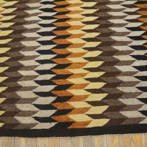 Flat-weave rug with brown, black, orange, and cream geometric pattern lying on wooden floorboards.