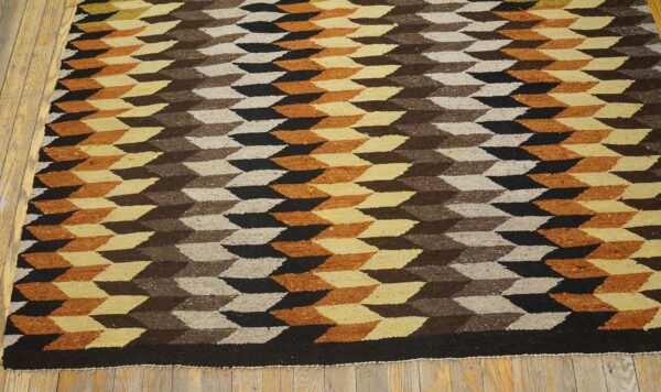 Flat-weave rug with brown, black, orange, and cream geometric pattern lying on wooden floorboards.