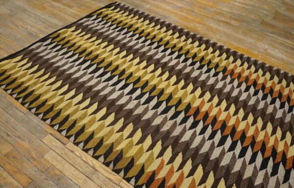 Low-pile rug with geometric brown, gold, black, and beige diamond patterns on wood flooring.