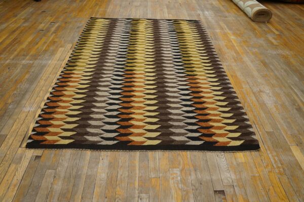 Flatweave rug featuring brown, yellow, black, and beige geometric blocks rests on worn wood flooring.