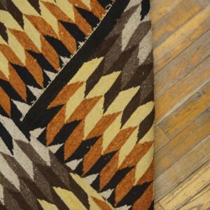 Low-pile rug with geometric diamonds in black, brown, beige, and burnt orange rests on a wood floor.