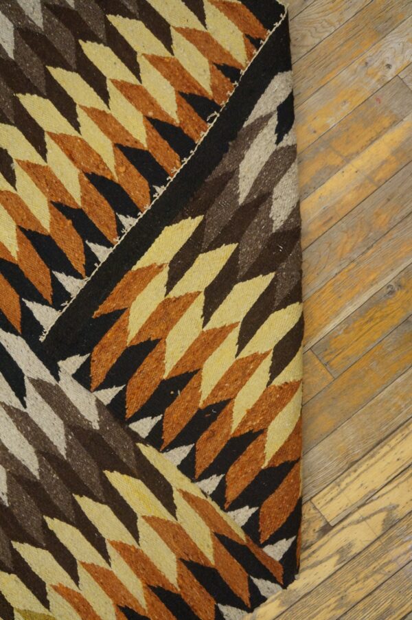 Low-pile rug with geometric diamonds in black, brown, beige, and burnt orange rests on a wood floor.