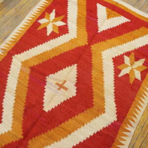 Geometric flatweave rug in red, orange, and cream with starburst designs on natural wood floors.