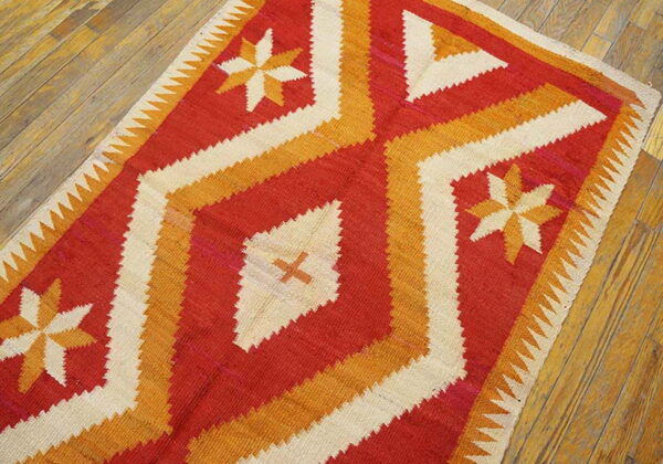 Geometric flatweave rug in red, orange, and cream with starburst designs on natural wood floors.