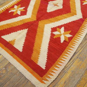 Red, gold, and white flatweave rug with geometric diamonds and star patterns on wide wood floors.