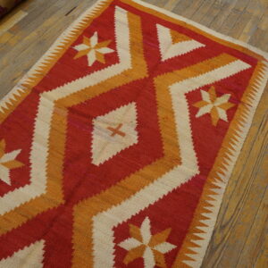Red, orange, and cream flatweave rug with geometric stars and diamonds lies on rustic wood flooring.