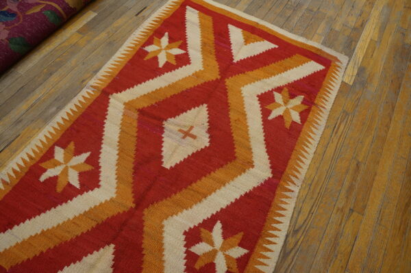 Red, orange, and cream flatweave rug with geometric stars and diamonds lies on rustic wood flooring.