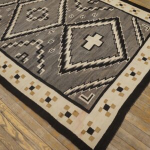 Gray and black geometric flatweave rug with a cream and tan border resting on wood planks.