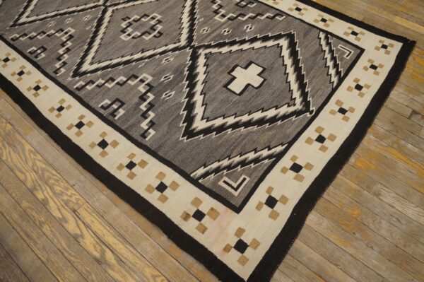 Gray and black geometric flatweave rug with a cream and tan border resting on wood planks.