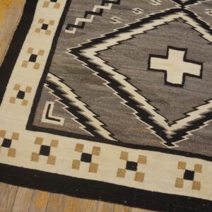 Geometric gray and black rug with a cream border lies on a distressed wooden floor with chipped yellow paint.