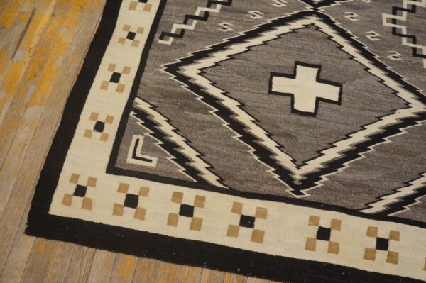 Geometric gray and black rug with a cream border lies on a distressed wooden floor with chipped yellow paint.
