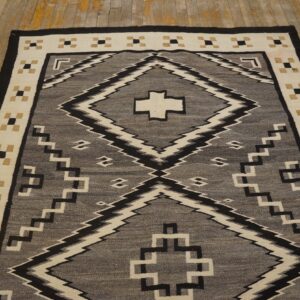 Geometric flatweave rug in gray, black, and cream colors laid on aged yellow wood floors.