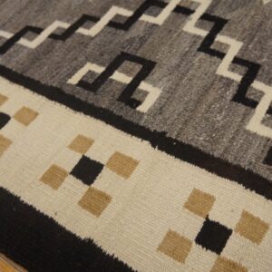 Flatweave rug detail showing geometric patterns in gray, black, and off-white over wooden floorboards.