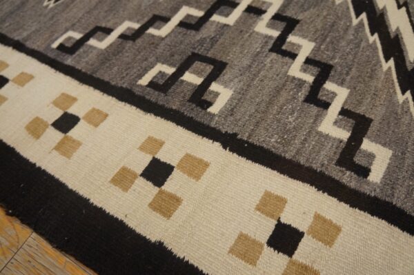 Flatweave rug detail showing geometric patterns in gray, black, and off-white over wooden floorboards.
