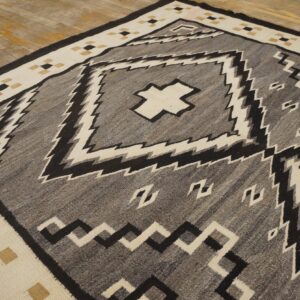 Flatweave rug featuring a gray, black, cream, and tan geometric pattern centered on distressed wood floors.