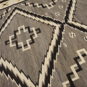 Gray and black rug with cream serrated diamonds and stepped geometric motifs on wood floor.