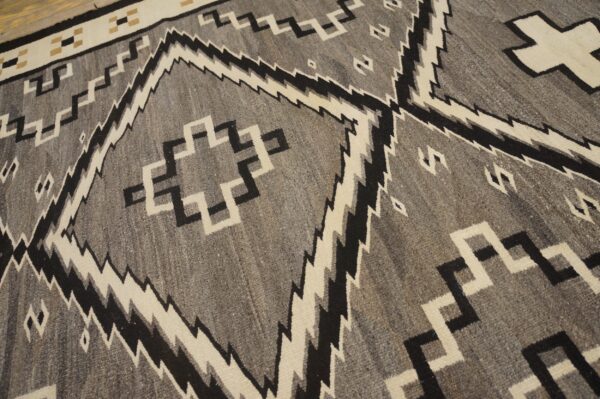 Gray and black rug with cream serrated diamonds and stepped geometric motifs on wood floor.