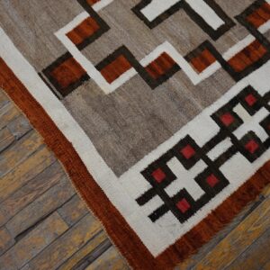Geometric flatweave rug in rust, gray, cream, and brown rests on worn wood plank flooring.