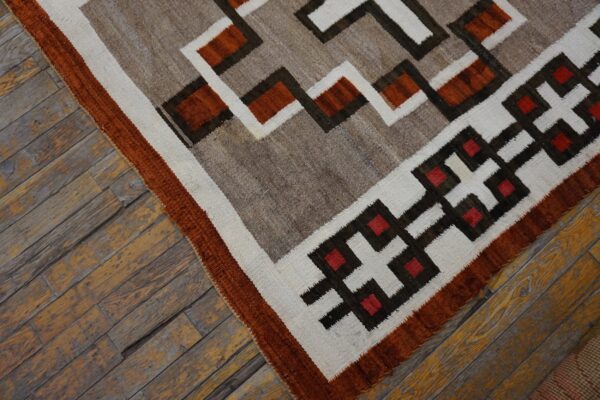 Geometric flatweave rug in rust, gray, cream, and brown rests on worn wood plank flooring.