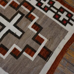 Flatweave rug with earthy geometric patterns in rust, tan, white, and dark brown on distressed wood planks.