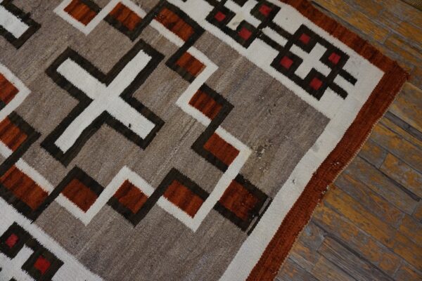 Flatweave rug with earthy geometric patterns in rust, tan, white, and dark brown on distressed wood planks.