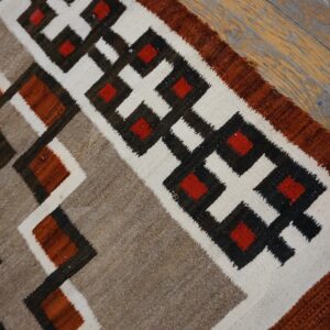 Geometric flatweave rug in red, brown, white, and tan featuring interlocking stepped patterns on distressed wood.