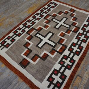 Geometric flatweave rug in neutral tones, brown, rust, and red rests on distressed gray wood flooring.