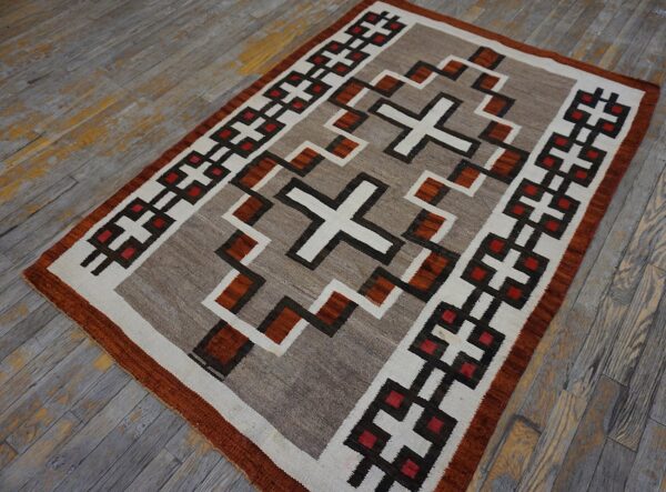 Geometric flatweave rug in neutral tones, brown, rust, and red rests on distressed gray wood flooring.