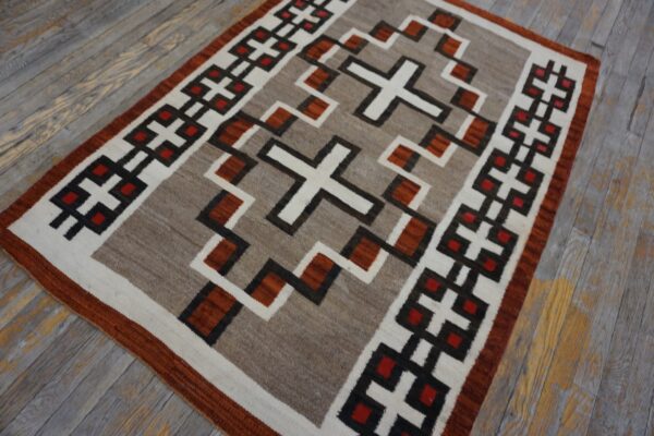 Tan and white geometric flatweave rug with dark brown and rust accents on weathered wood flooring.