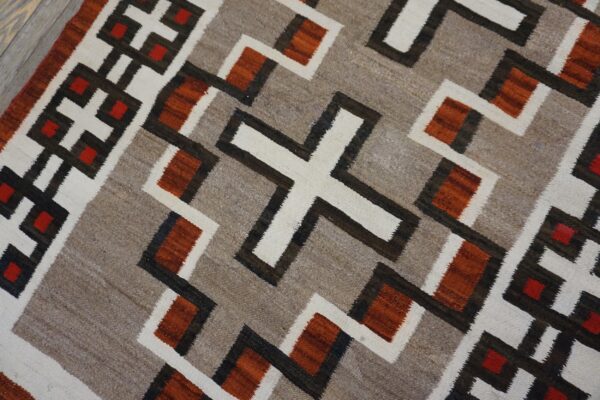 Low-pile geometric rug in taupe, off-white, dark brown, rust, and red on light wood flooring.