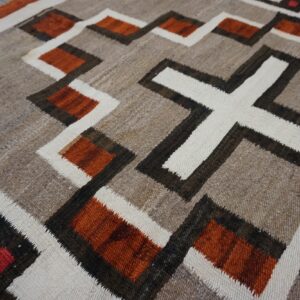 Rustic flatweave rug in natural browns, cream, rust, and black geometric patterns on wood flooring.