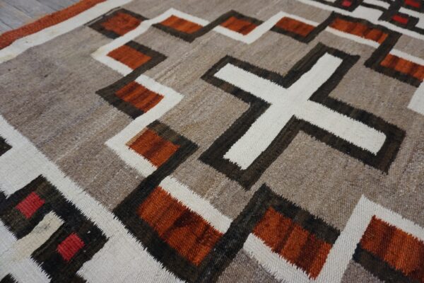 Rustic flatweave rug in natural browns, cream, rust, and black geometric patterns on wood flooring.