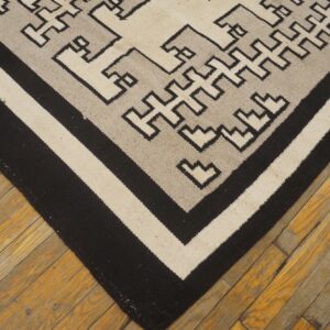 Black, cream, and gray geometric flatweave rug lying on aged amber wood floorboards.