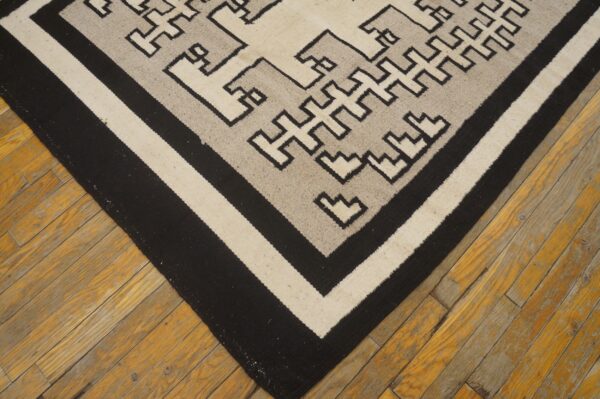 Black, cream, and gray geometric flatweave rug lying on aged amber wood floorboards.