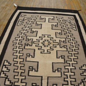 Black, gray, and beige flatweave rug featuring a complex geometric central design on distressed wood floors.