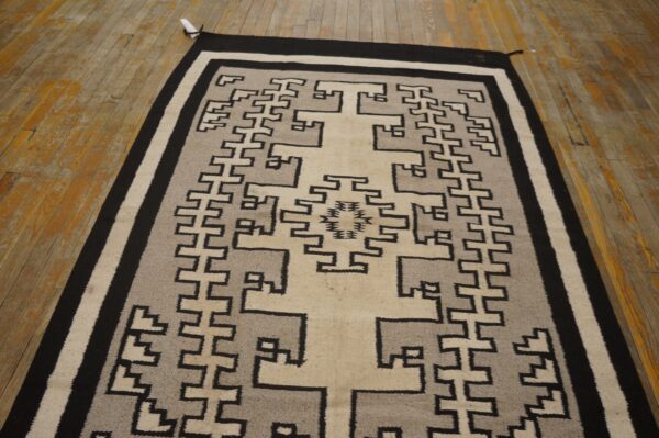 Black, gray, and beige flatweave rug featuring a complex geometric central design on distressed wood floors.