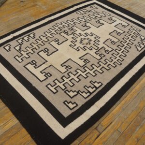 A flatweave rug with a black, beige, and gray geometric step pattern rests on distressed wooden floorboards.