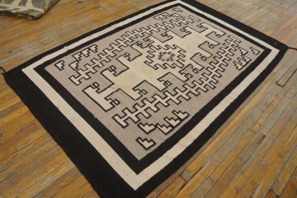 A flatweave rug with a black, beige, and gray geometric step pattern rests on distressed wooden floorboards.