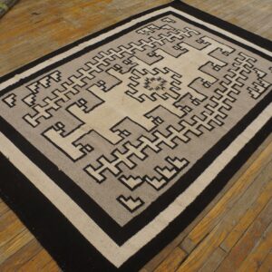 Geometric black, gray, and cream flatweave rug featuring interlocking key motifs on distressed wood flooring.