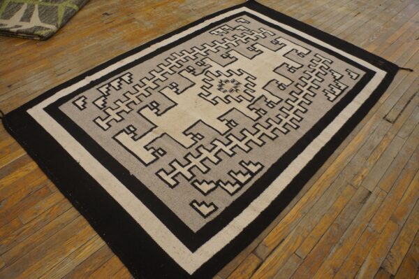 Geometric black, gray, and cream flatweave rug featuring interlocking key motifs on distressed wood flooring.