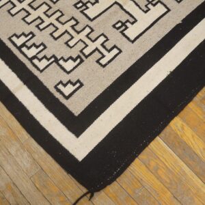 Flatweave rug in black, gray, and cream with geometric patterns rests on distressed wooden floorboards.