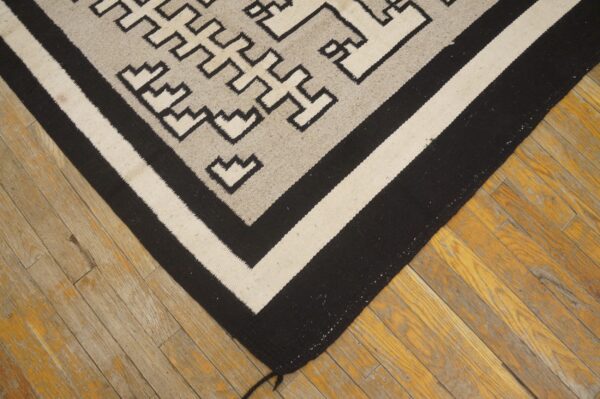 Flatweave rug in black, gray, and cream with geometric patterns rests on distressed wooden floorboards.
