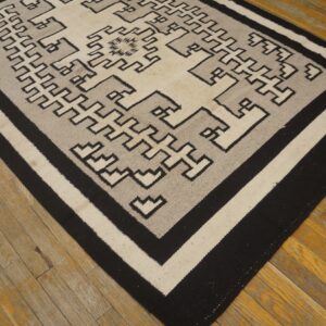 Black, gray, and cream geometric flatweave rug resting on distressed hardwood planks.