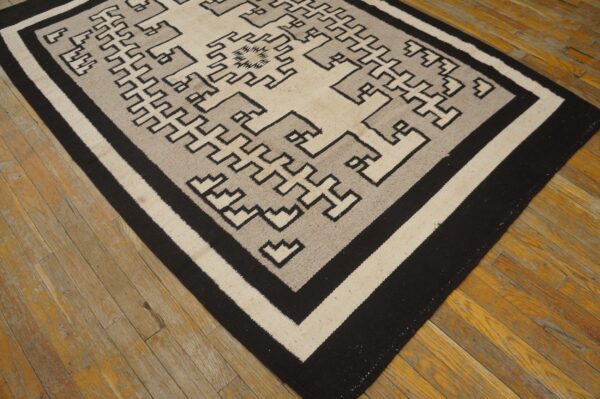 Black, gray, and cream geometric flatweave rug resting on distressed hardwood planks.