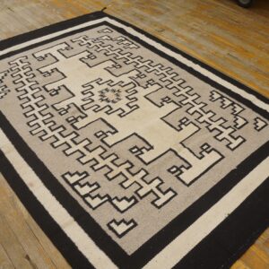A black, cream, and gray flatwoven geometric rug rests on an aged wooden floor.