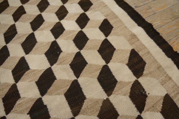 Low-pile rug with a tumbling block pattern in dark brown, beige, and cream colors on light wood floors.