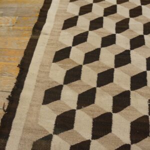 Dark brown and beige flatweave rug with an optical cube pattern on rustic wooden flooring.